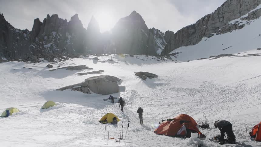 People camp near trees at the base of mountains in the snow