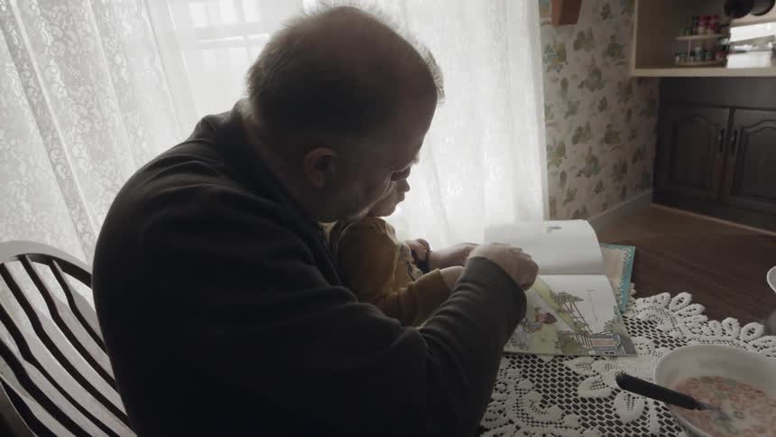 Grandfather and grandson sitting at table reading book