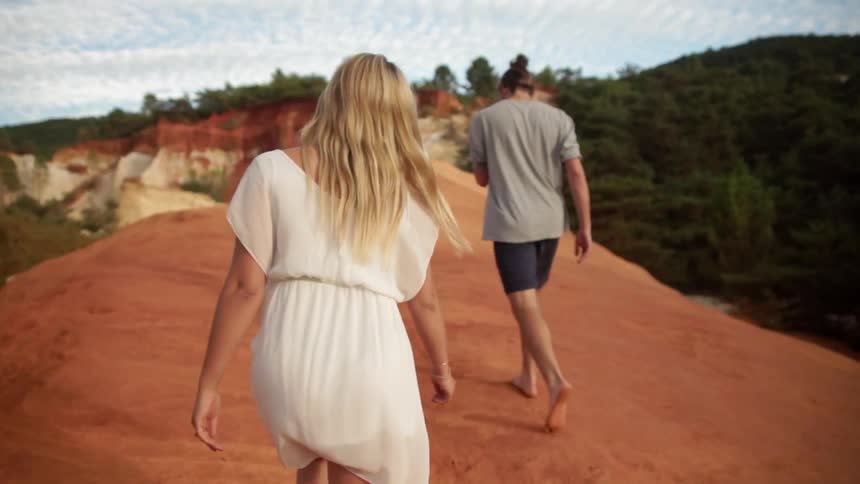 Man and woman walk outside on a sandy hill near trees
