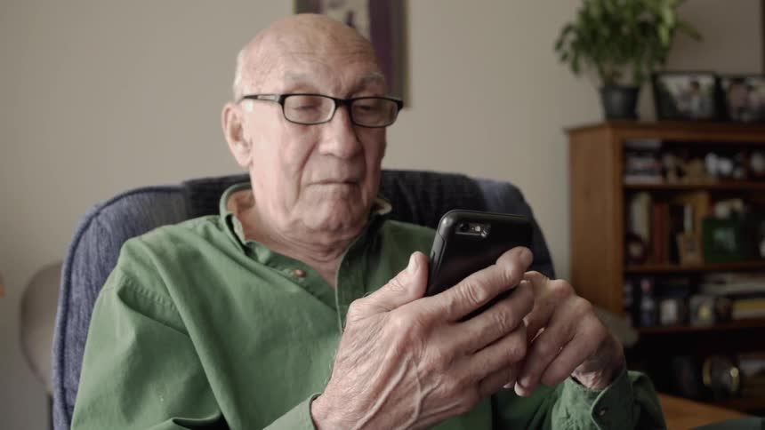 Elderly man sits in a chair looking at a phone