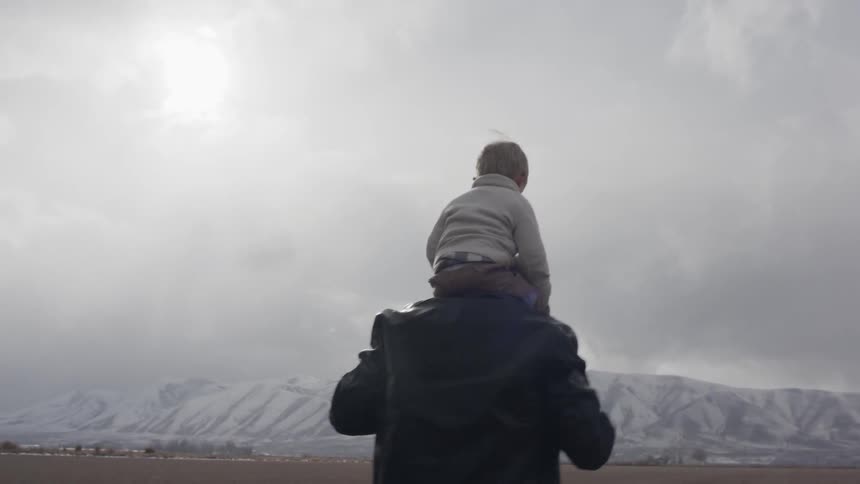 A man with a boy on his shoulders points and gestures as he walks
