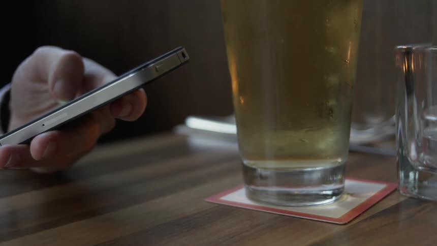 A hand picks up a phone next to a glass of beer