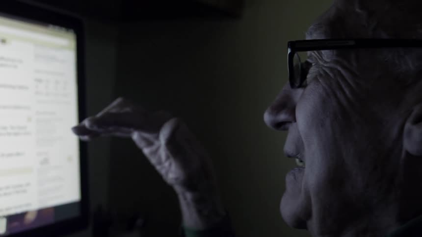 Elderly man talks and looks at a computer monitor