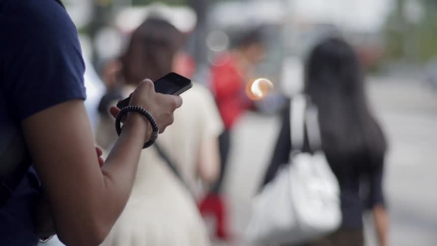 A man is standing on a city sidewalk using a cellphone in daylight