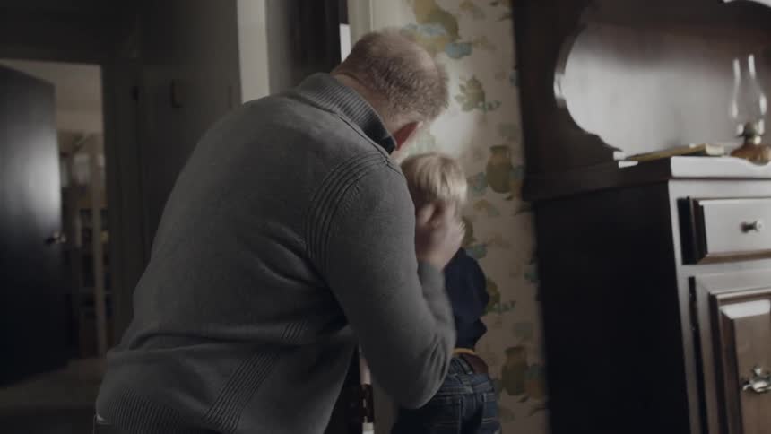 Toddler stands near a wall as a man marks his height