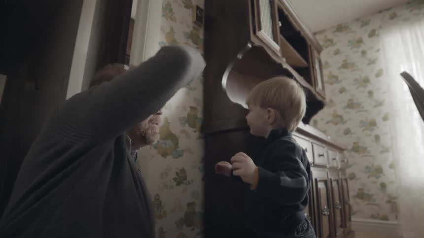 Elderly man tries to measure a toddler against a wall but the toddler runs away