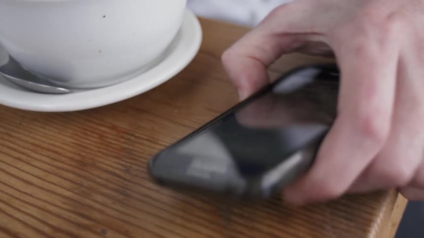 Man picks up his phone while drinking coffee