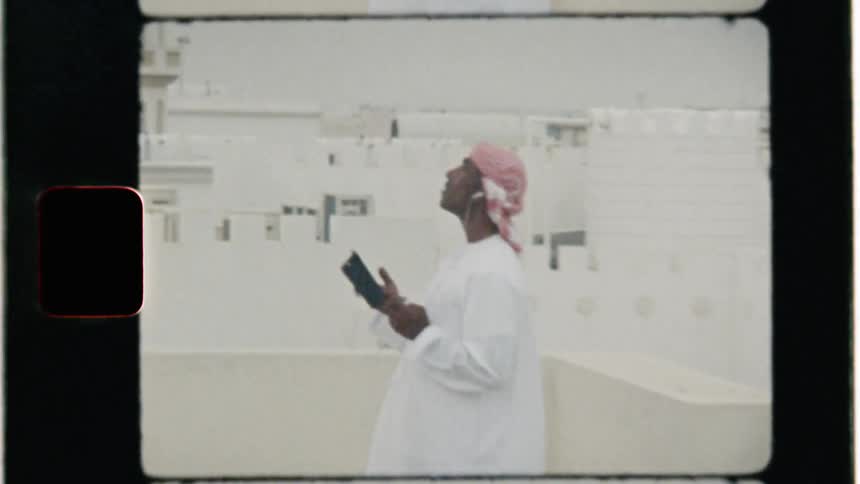 An arab man is standing on a rooftop talking on his cellphone in daylight