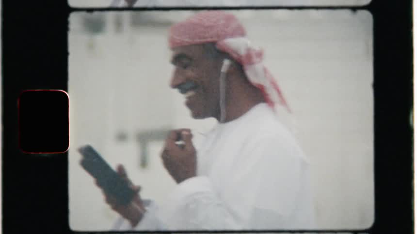 Man wearing head wrap is laughing while video chatting on cell phone outside
