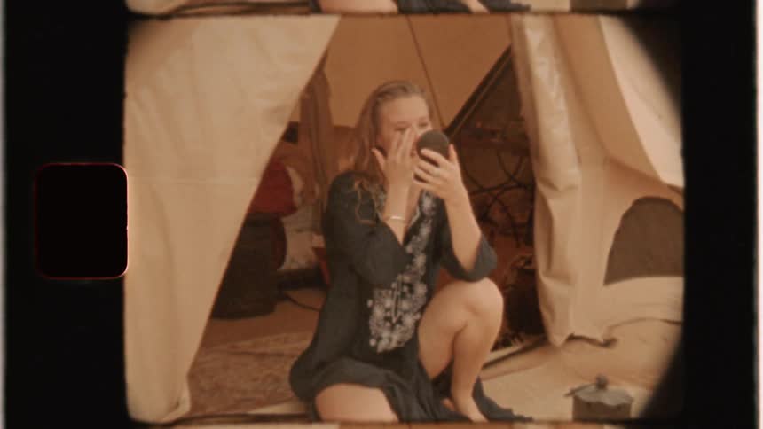 Woman sits in a tent looking at herself in a mirror