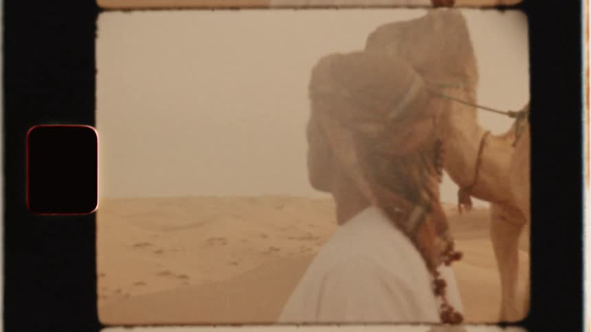 A man stands in the desert with men riding camels
