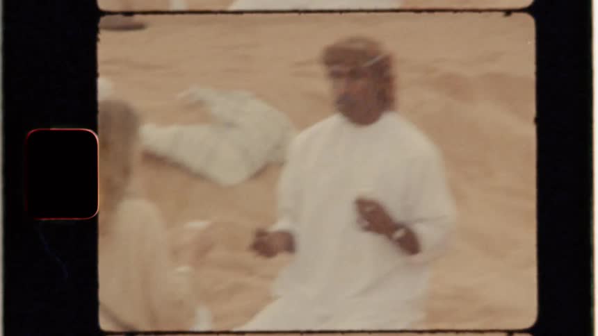 Two men and a woman sit on the sand in a desert
