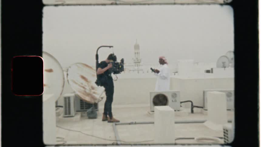 Man with movie camera films man standing on roof