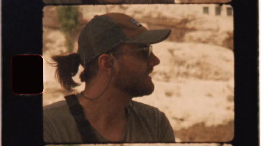 Man in a hat and glasses talks and motions with his hands