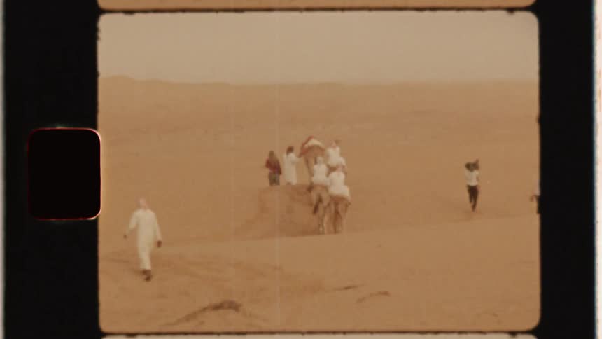 A man is leading a caravan of camels across sand dunes in daylight