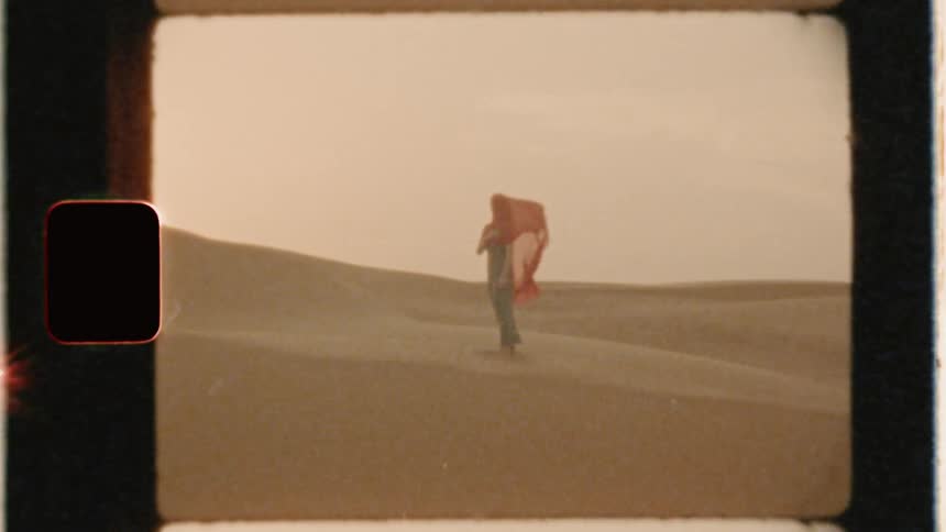 A woman stands in the desert as the wind blows her scarf