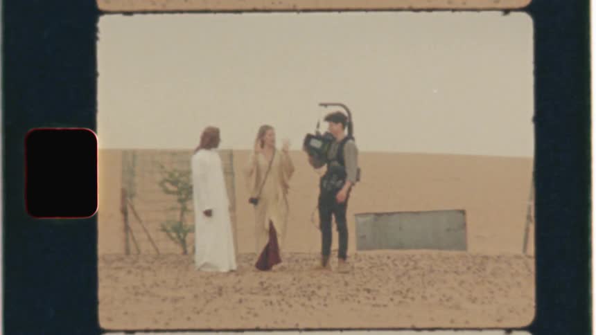 Man with movie camera talks to another man and woman