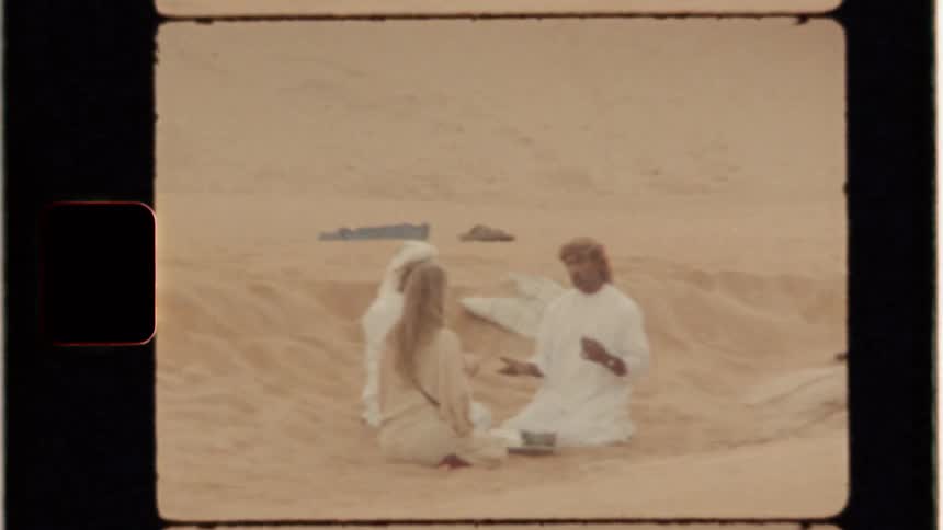 A woman sits in the sand with two arab men talking