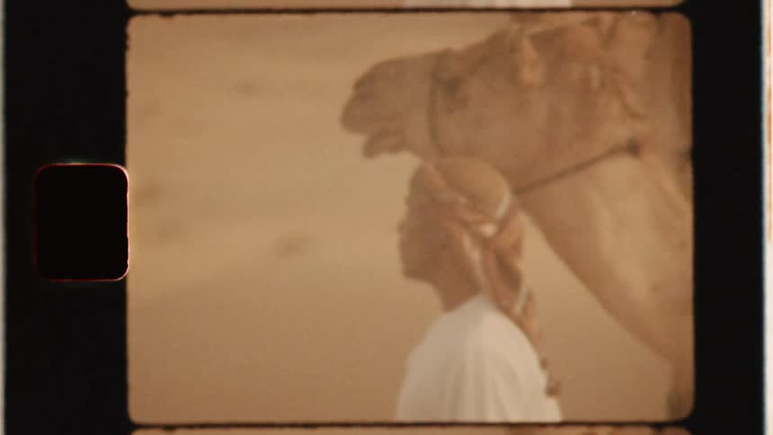An arab man stands beside a camel in the desert