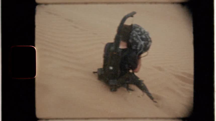 A man is being pelted by blowing sand as he films in the desert in daylight