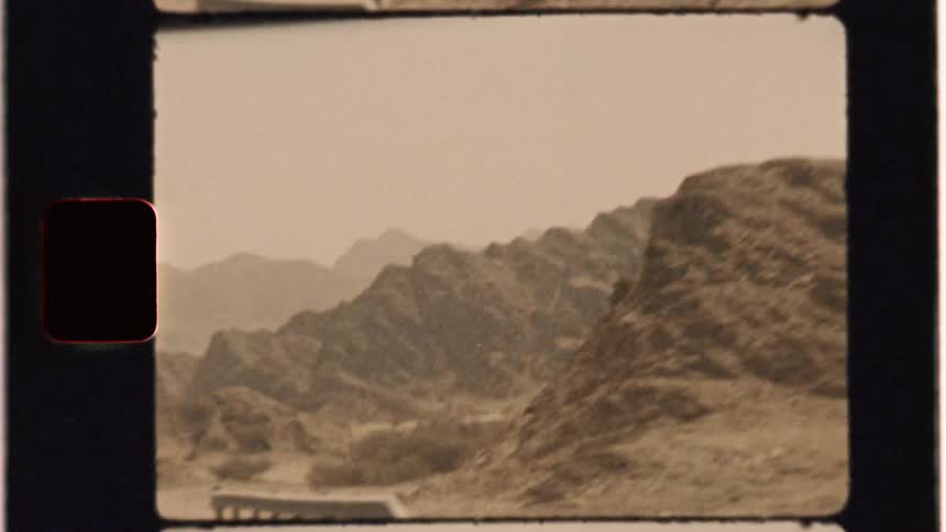 A car drives by rocky mountains in a desert