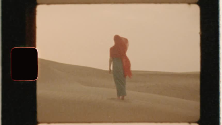 Woman wearing a red cloth on her head stands in a sandy desert