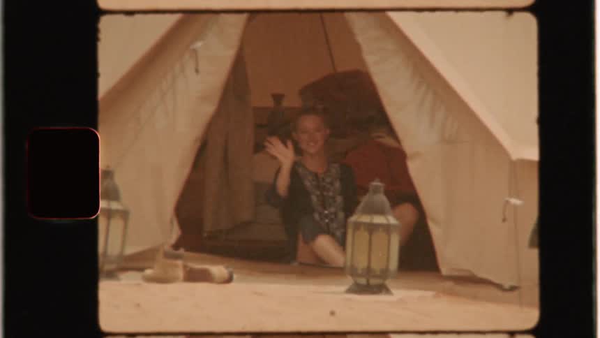Woman smiles and waves while sitting in a tent in the desert