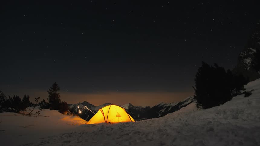 Light glows inside a tent on a snow covered clearing