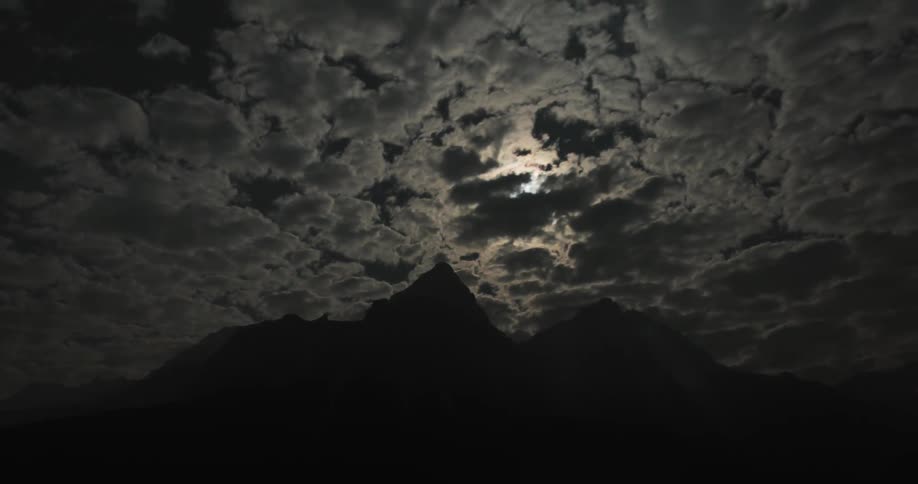 Clouds pass above the mountain with the moon generating rays of light