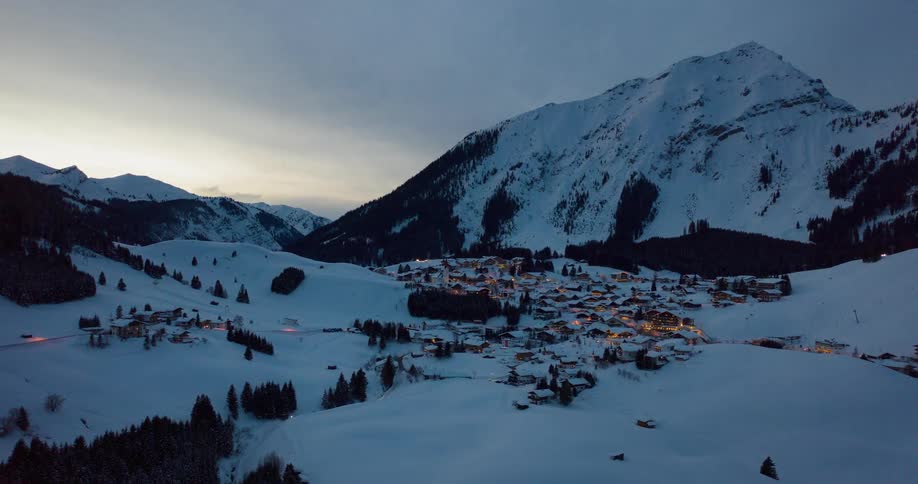 A town sits nestled in snowy mountains at sunset