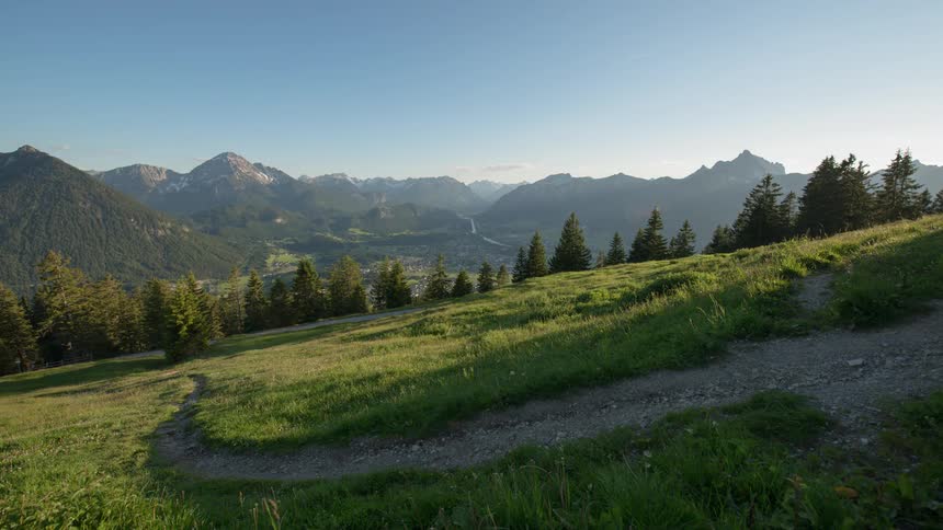Sun sets over a path winding through grass leading to mountains