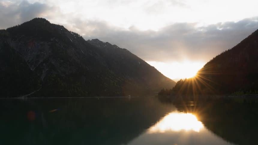 Clouds are passing over hills near a lake as dawn breaks