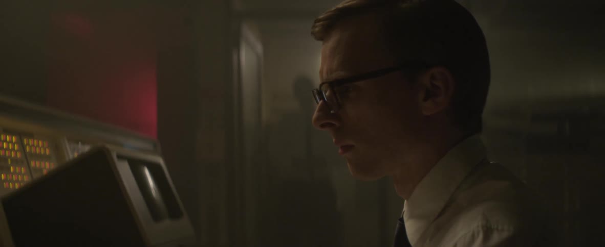 A man enters data into an old computer while a man looks on from the doorway