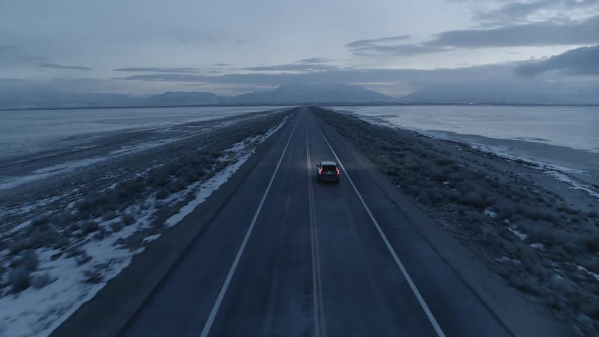 Car drives down a snowy country road at sunrise