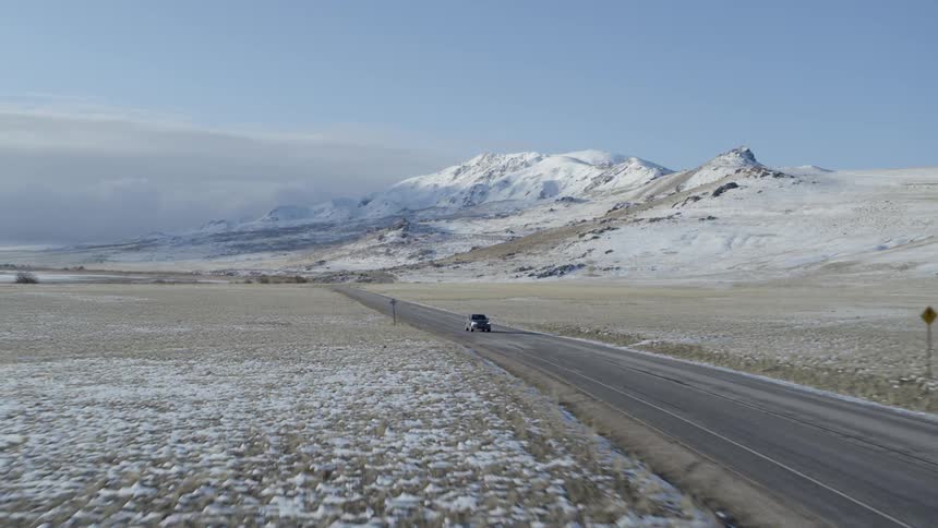 A truck drives down a rural road by a mountain