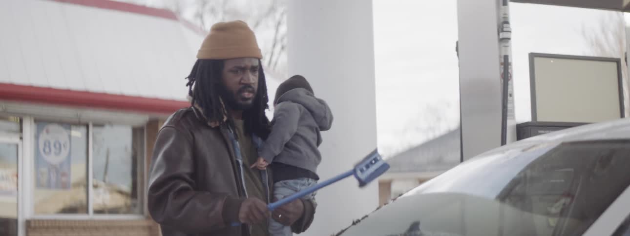 Man holds a child while he scrapes ice off his car windshield