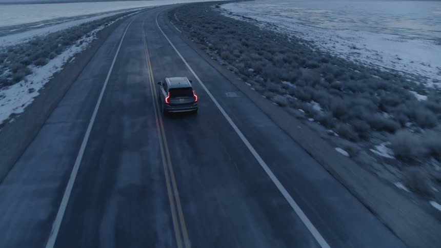 An SUV tail lights glow as it travels on a coastal road on a gray winter day