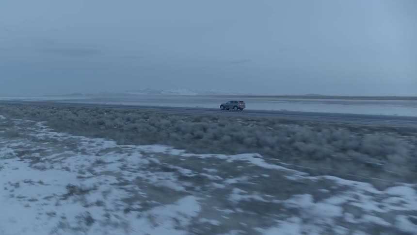 Car drives down a snowy country road on a cloudy day