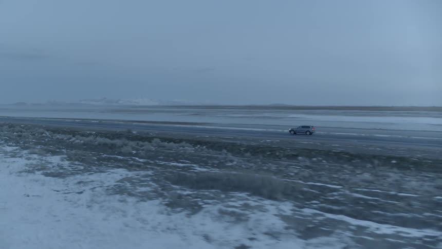 Vehicle travels down the road between a field and the ocean