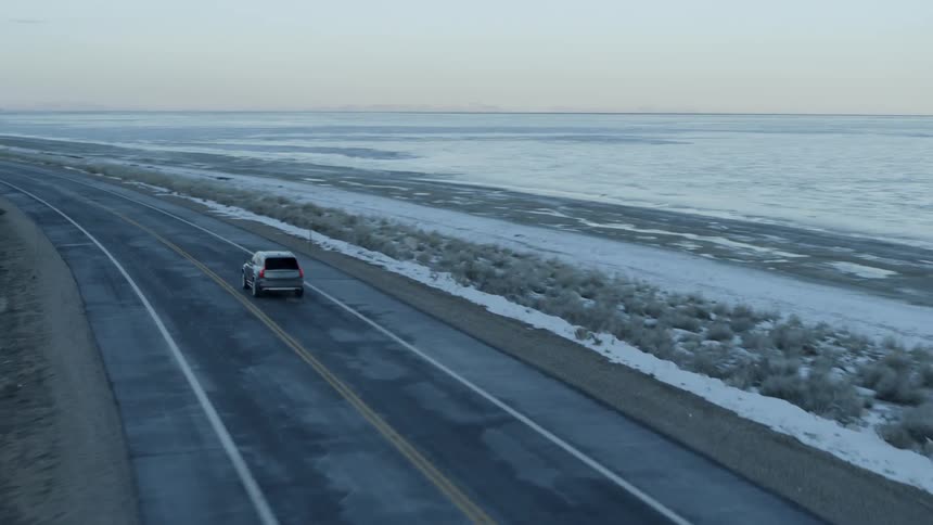 Car drives down a country road in the winter next to a large body of water