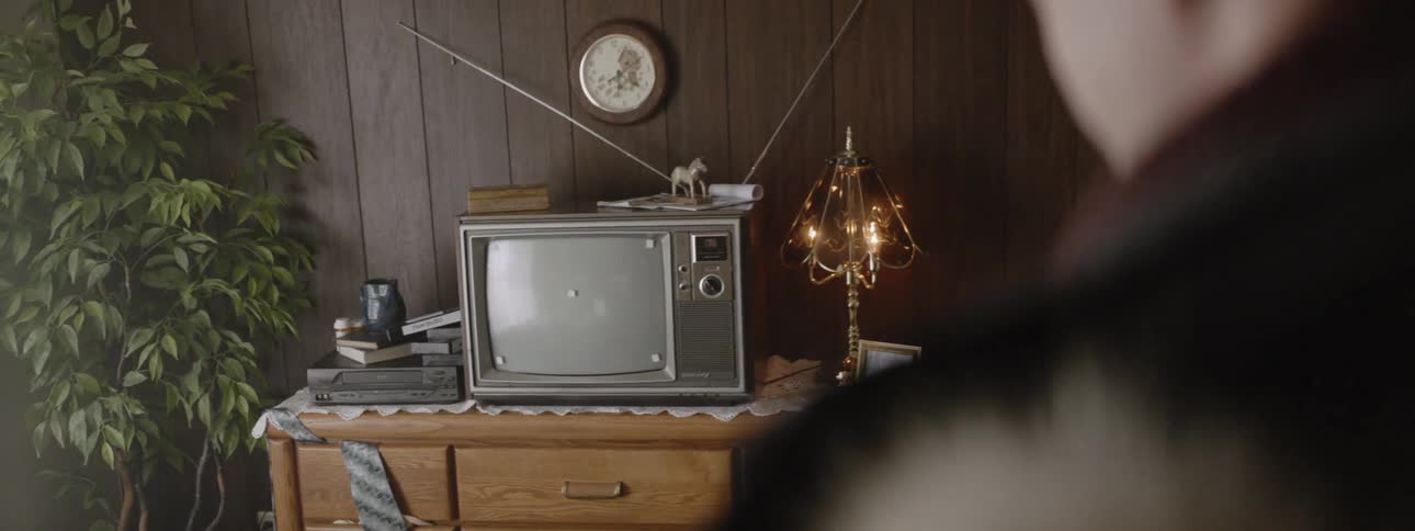 A man is standing inside a home looking at a television in daylight