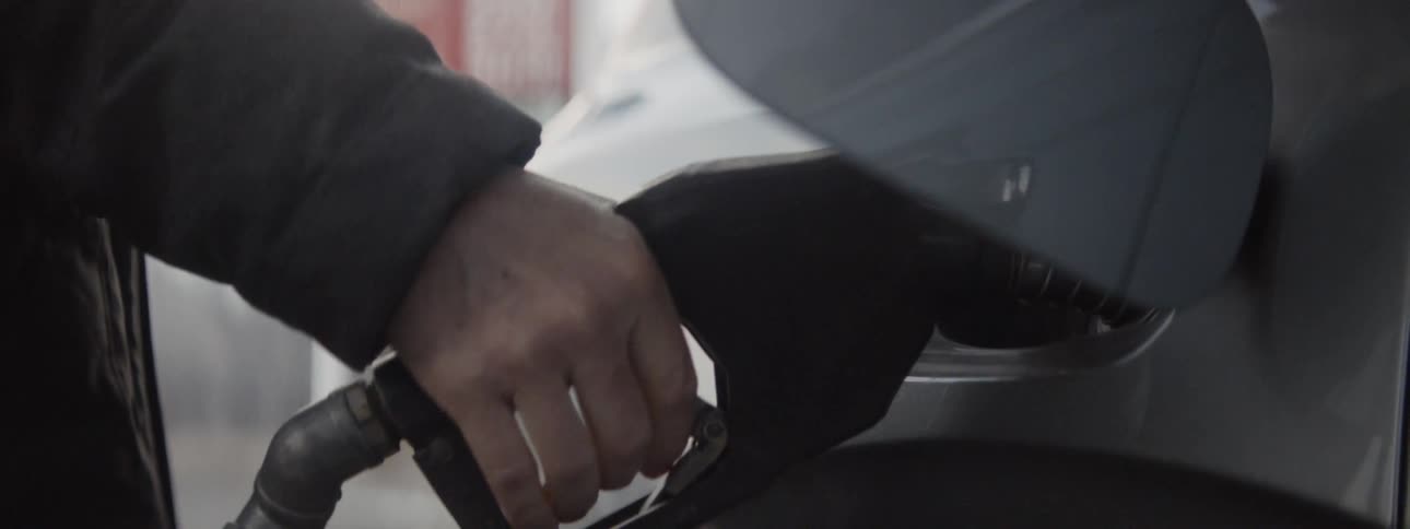 A man pops open the gas tank lid on a car and pumps gas