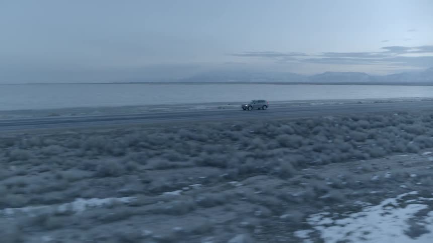 Car drives down a road next to a body of water and snowy ground