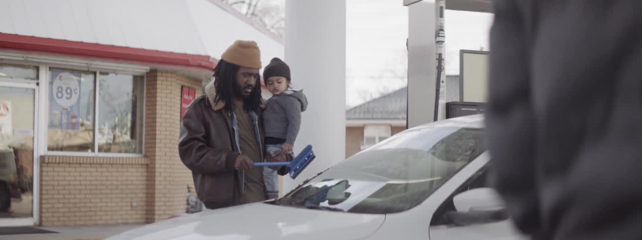 Man holds a small child while cleaning the windshield of his car