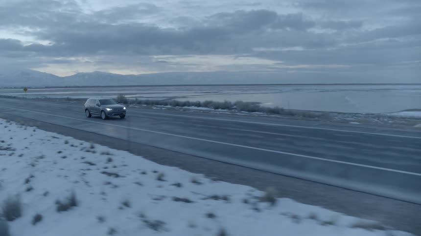 Car drives down a road next to a large body of water in the winter