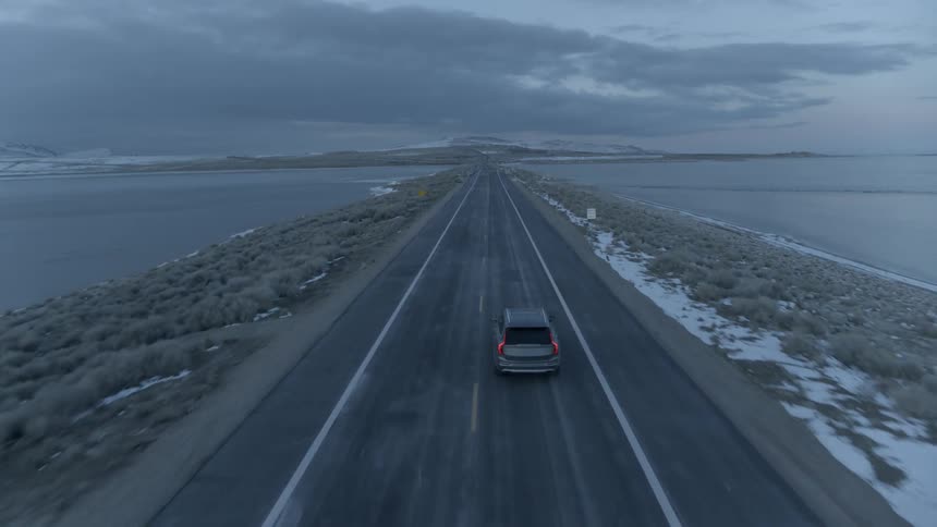 Car drives on a lakeside road at dusk