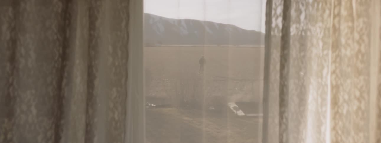 Curtain over a window and a man standing outside in a field