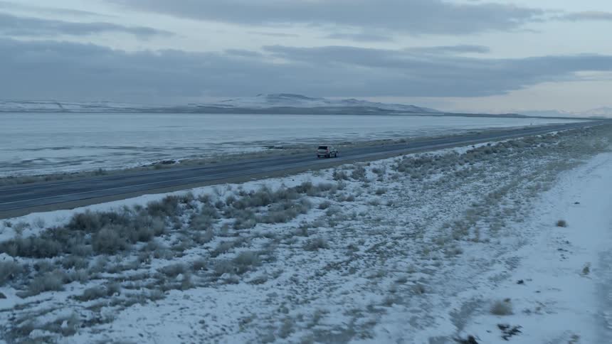 A car travels on a rural snowy road at sunset