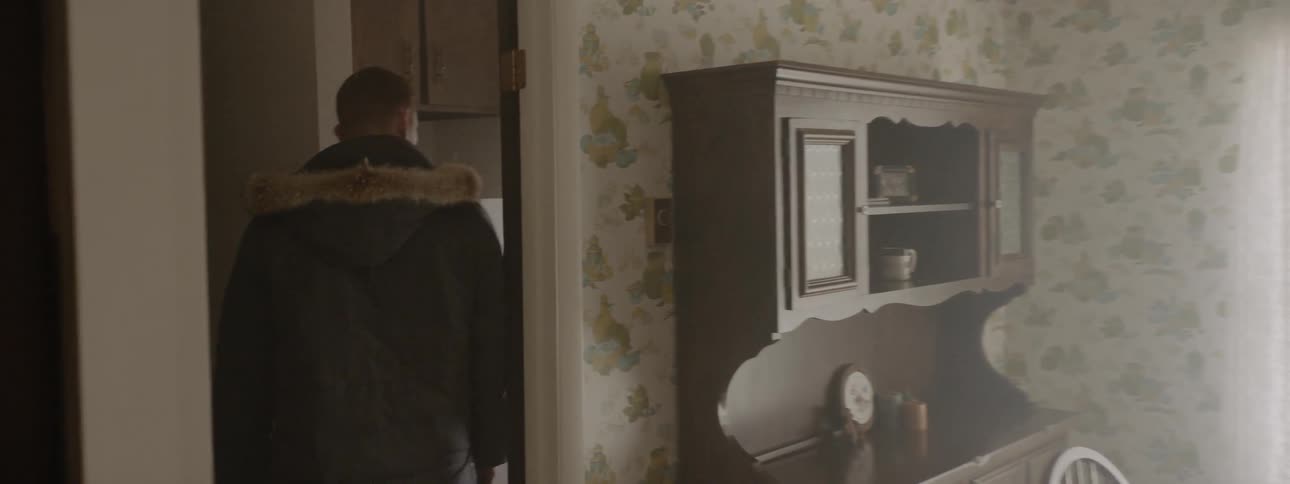 A man walks through a dining area and enters a pantry in a house