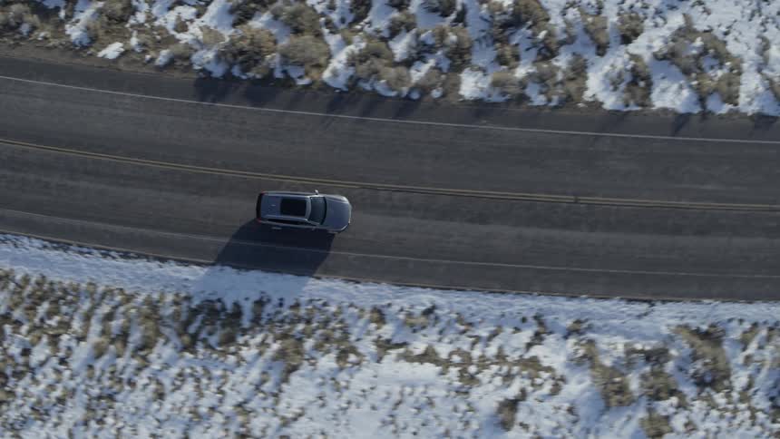 A car drives on a road lined with snow